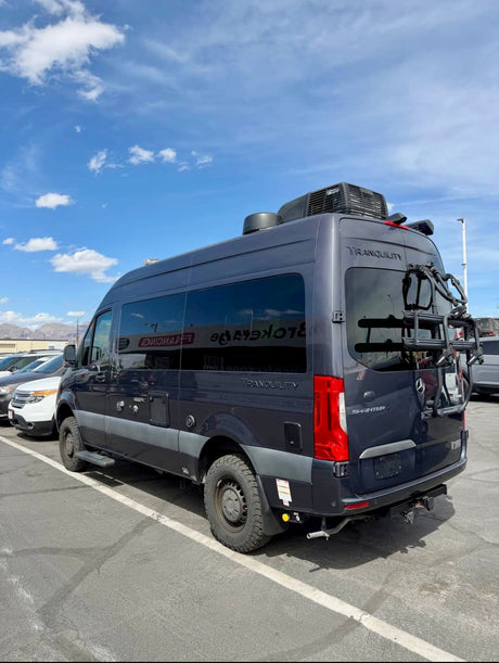 Dark blue Mercedes Sprinter Tranquility camper van, an RV rental, with a bike rack & roof AC, ready for outdoor adventures.