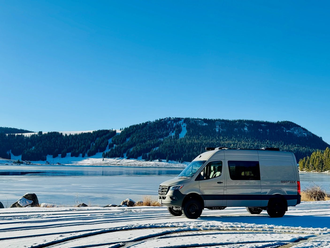 Experience winter in style! This GEOTREK camper van, ideal for your next rv rental adventure, by a frozen lake and snowy mountains.