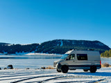 Experience winter in style! This GEOTREK camper van, ideal for your next rv rental adventure, by a frozen lake and snowy mountains.