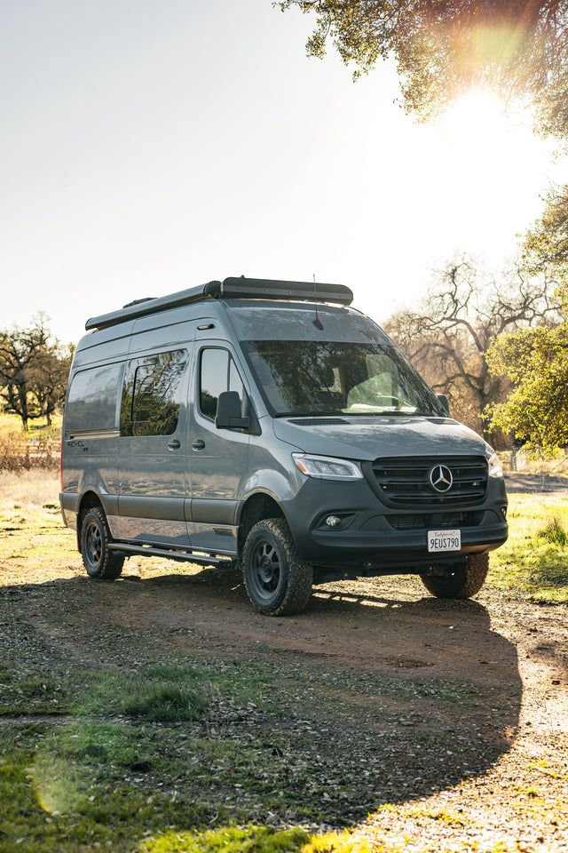This sleek gray Mercedes-Benz Sprinter RV rental, a Winnebago Revel, is parked on a sunlit dirt path, ready for adventure.