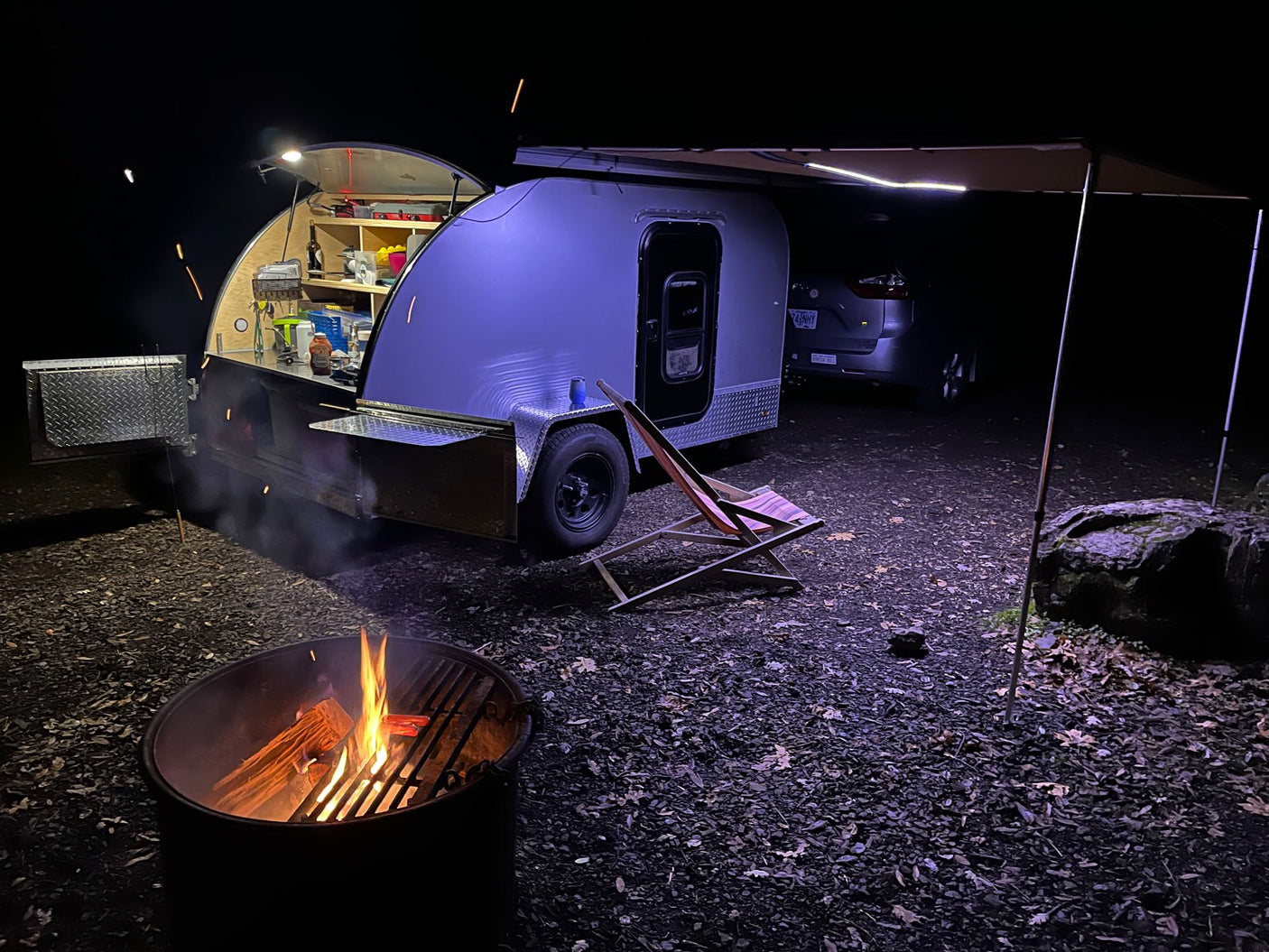 Night camping with a cozy RV rental teardrop trailer, campfire, and ambient lights. Perfect outdoor adventure.