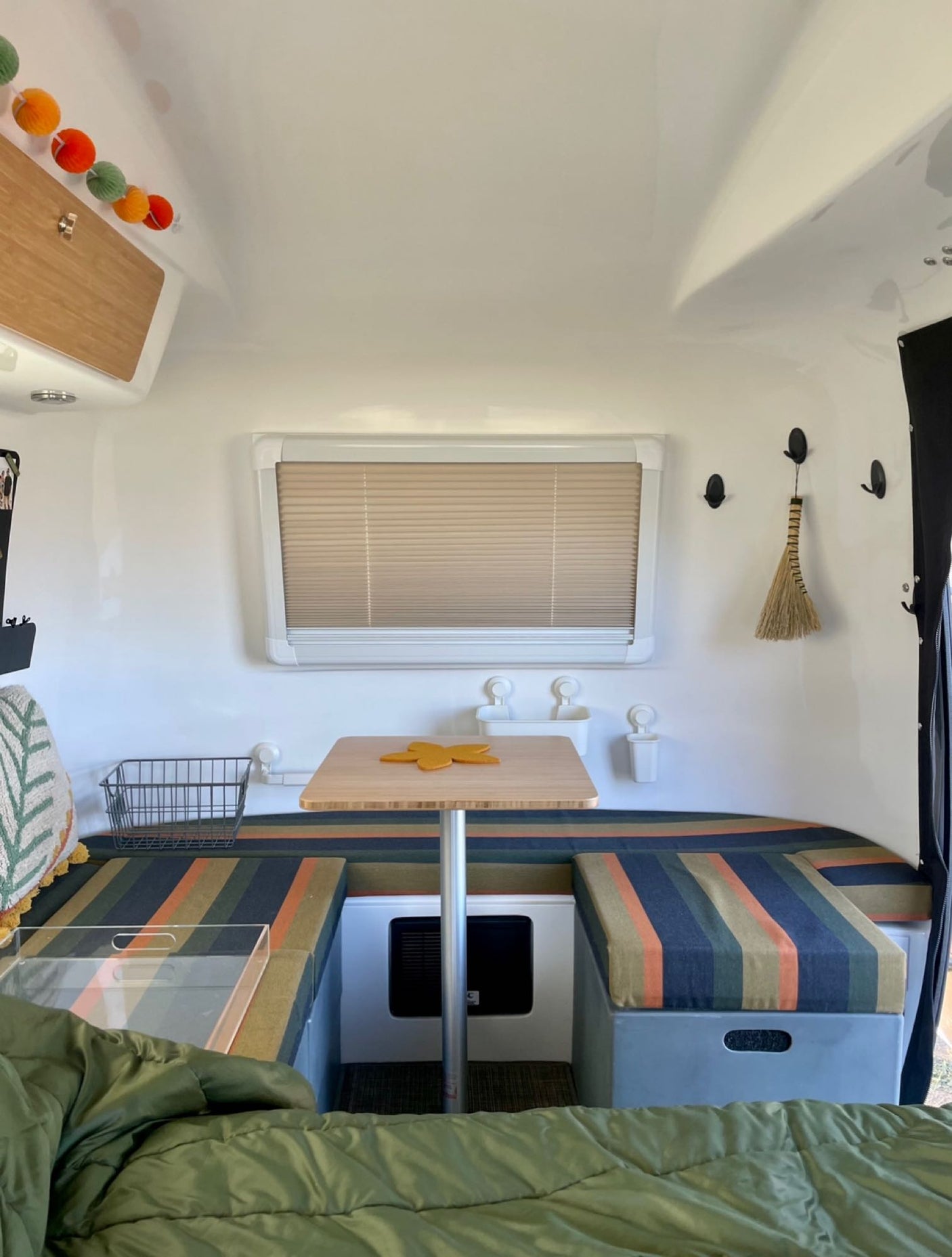 View inside a cozy RV rental, showing the compact dinette area with striped cushions, table, and bed. Ideal for travel.