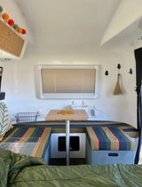 View inside a cozy RV rental, showing the compact dinette area with striped cushions, table, and bed. Ideal for travel.