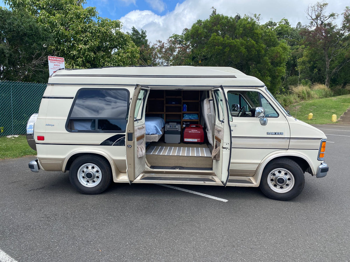 Beige Dodge Ram conversion van with open doors, showing its interior bed and shelves. Parked outside, resembling an RV rental. — photo 13