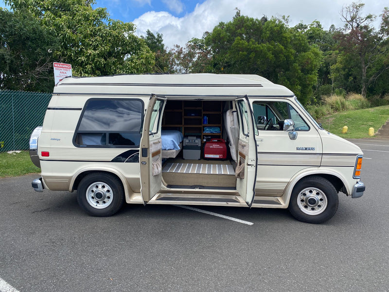 Beige Dodge Ram conversion van with open doors, showing its interior bed and shelves. Parked outside, resembling an RV rental. — photo 13
