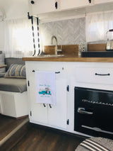 Bright rv rental kitchen featuring wood counters, white cabinets, a chevron backsplash, and a black Frigidaire fridge.