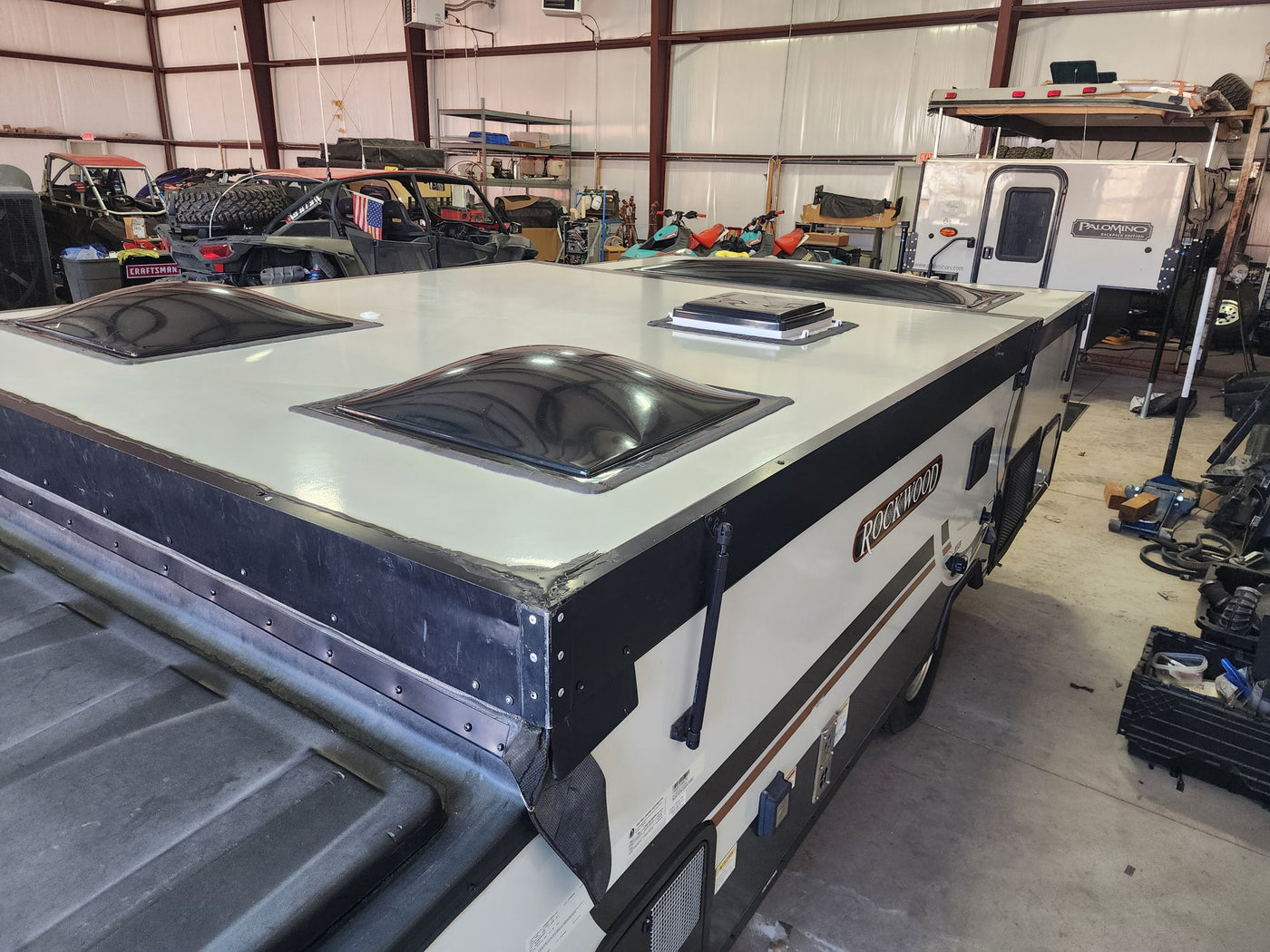 A Rockwood pop-up camper's roof with skylights, ideal for an RV rental. Workshop scene with UTVs, jet skis, & a Palomino camper. — photo 13