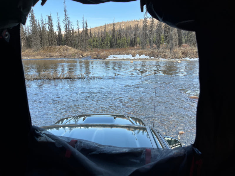 View from an RV rental's window: a vehicle crossing a shallow river, surrounded by a winter forest. — photo 4