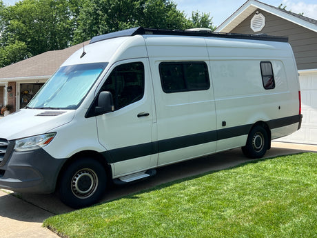 A white Mercedes Sprinter camper van for RV rental, parked on a sunny driveway, ready for adventure travel.