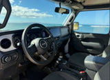 Inside a Jeep, the steering wheel and dashboard are visible. Beyond the windshield, a bright blue sky and turquoise ocean. Great for your RV rental adventure.