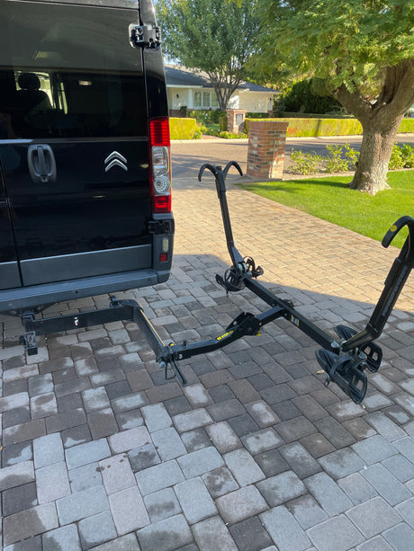 Black Citroën RV rental van with a platform hitch bike rack attached, parked on a paver driveway. Ready for trips.