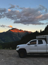 Enjoy a scenic RV rental trip! White truck camper at sunset with a moonlit mountain and forest backdrop.