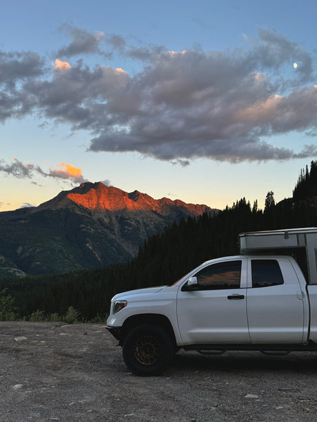 Enjoy a scenic RV rental trip! White truck camper at sunset with a moonlit mountain and forest backdrop.