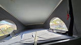 Inside an RV rental's pop-up tent, showing the bed area and side windows with outside views.