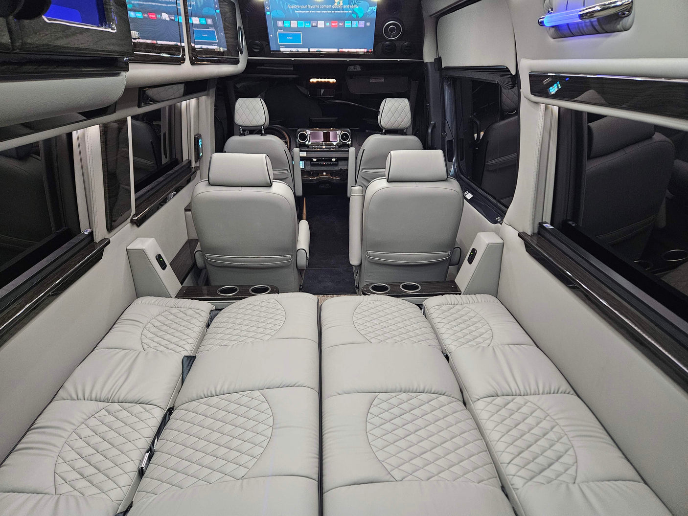 Luxury van RV rental interior: Light gray quilted seating converts to a bed, with screens and cup holders.