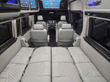 Luxury van RV rental interior: Light gray quilted seating converts to a bed, with screens and cup holders.