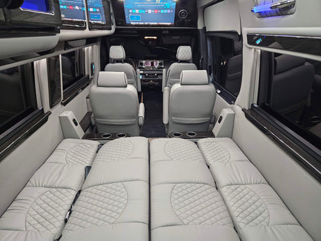 Luxury van RV rental interior: Light gray quilted seating converts to a bed, with screens and cup holders.