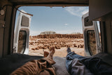 RV rental adventure: Two people relax with feet up, admiring the vast desert landscape and unique rock formations from their van.
