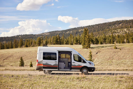 White camper van on a dirt road amidst mountains, perfect for your next rv rental adventure.