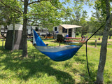 Enjoying a bright RV rental campsite. A blue/gray hammock hangs between trees, with two RVs, a tent, and picnic table nearby.