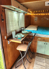 Cozy RV rental interior with dining area for two, a comfortable bed, and charming decor.