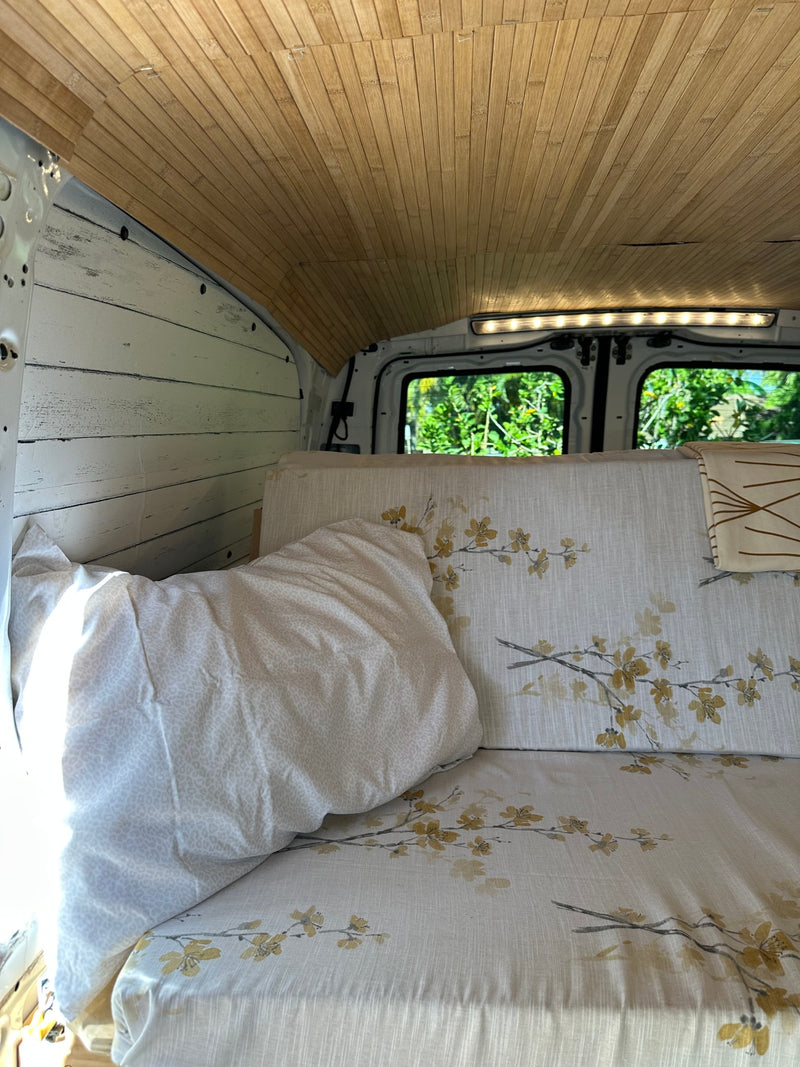 Cozy RV rental interior featuring a wood-slat ceiling, white paneling, floral bed, and bright rear window view. — photo 9