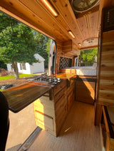 Inside a beautiful custom wooden camper van, offering rv rental comfort with a kitchen, stove, sink, bed, and scenic view.