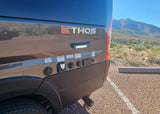 Grey Ethos RV rental's utility panel and rear tire visible, parked in gravel with desert mountains in the background.