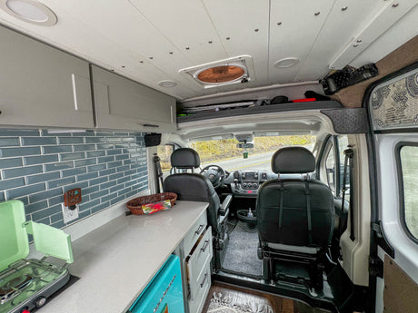 RV rental: Bright camper van interior with a compact kitchen, overhead storage, and front cockpit. Ready for your next trip!