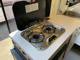 Inside an RV rental: a compact kitchen with a two-burner stove, sink, and countertop. Ideal for adventurers.