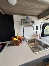 Compact RV rental kitchen with a stainless steel sink, fresh fruit bowl, and hand soap on a light counter.
