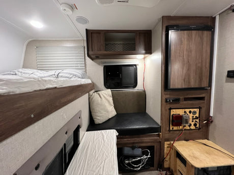 Cozy RV rental interior with bunk bed, dinette, compact fridge, and a custom power management display.