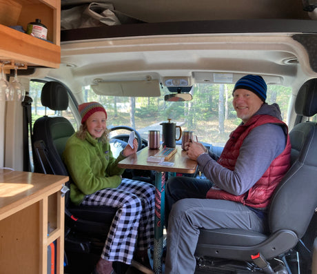 Smiling man and teen enjoy coffee and games in their RV rental. Cozy camper van interior for travel.