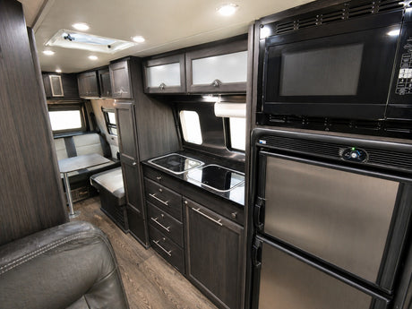 Modern RV rental interior features dark wood kitchen cabinets, stove, sink, microwave, fridge, and dining booth seating.