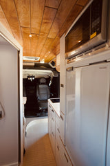 This RV rental offers a compact, modern interior with a wood ceiling, kitchenette, microwave, fridge, and a shower area.