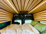 Modern RV rental bedroom featuring sleek wood paneling, ambient LED lighting, and a cozy bed with green pillows.