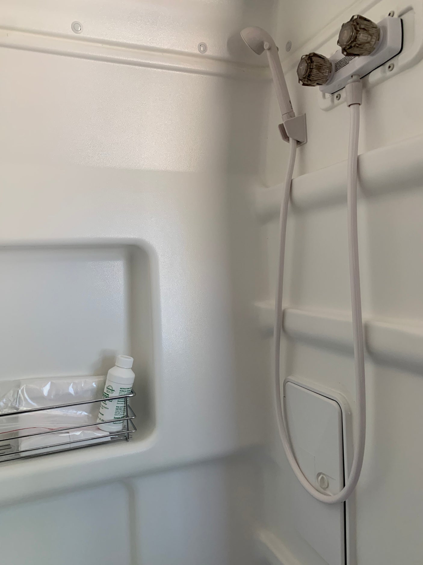 Compact white RV rental bathroom shower with handheld head, water controls, and basic toiletries on a rack.