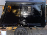 Custom-built black RV rental: a compact camper trailer with a window, wheel, and sturdy jack support.