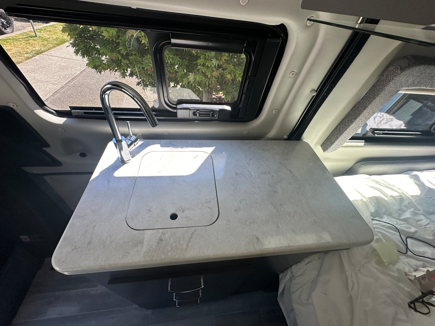 RV rental interior: functional kitchen counter with covered sink, modern faucet, window view, and comfortable bed.