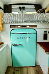 RV rental interior features a prominent retro aqua Galanz mini-fridge, cozy bed, and clever compact living space.