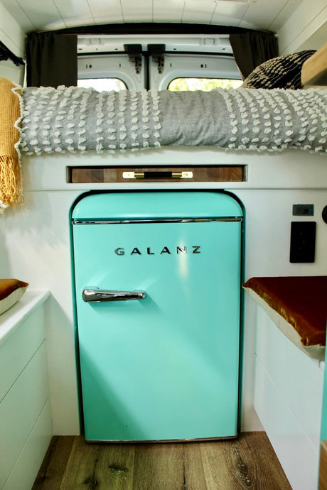 RV rental interior features a prominent retro aqua Galanz mini-fridge, cozy bed, and clever compact living space.