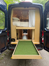 RV rental: Camper van interior shows bed, storage, and a unique pull-out artificial grass ramp extending from the rear.