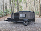 Dark gray Hiker teardrop camper parked at a wooded campsite, ready for your next RV rental adventure.