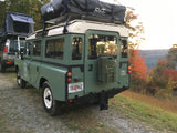 Classic green Land Rover with rooftop tent and jerry can, ready for rv rental adventures in autumn mountains.