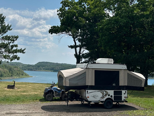 Pop-up camper RV rental & ATV by a scenic lake with forested hills. Perfect for camping and outdoor adventures.|A white pop-up camper