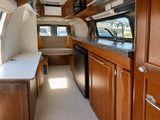 Interior of an RV rental: Features a kitchenette with sink, refrigerator, and a comfortable rear sofa/bed. Wood cabinetry.