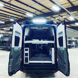 Inside a blue campervan, the rear doors open to reveal modular storage, a bed platform, and floor tracks, ready for RV rental adventures.