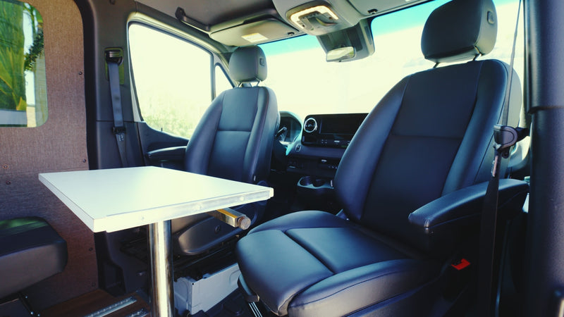 RV rental interior: two black front seats, a white table with chrome leg, and dashboard details visible, shot from the rear cabin. — photo 9