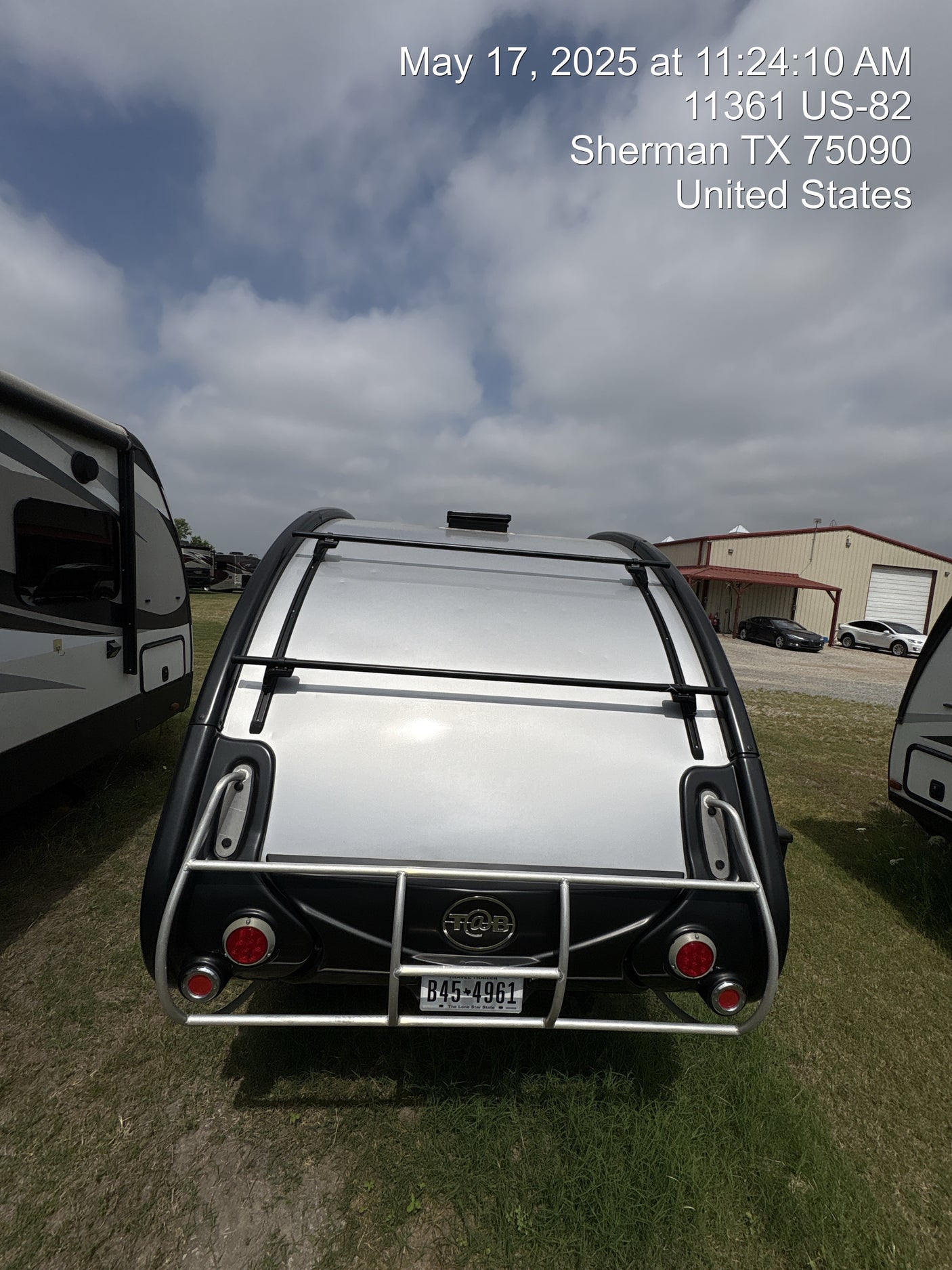 Rear of a silver T@B travel trailer, an RV rental unit, parked on grass at an RV lot in Sherman, TX.