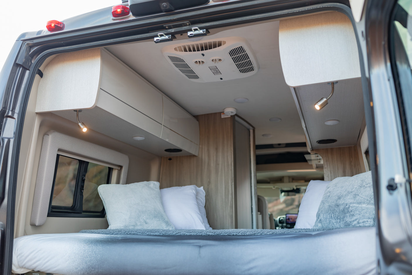 Explore the comfortable interior of this RV rental, featuring a plush bed, overhead cabinets, and AC for a relaxing journey.